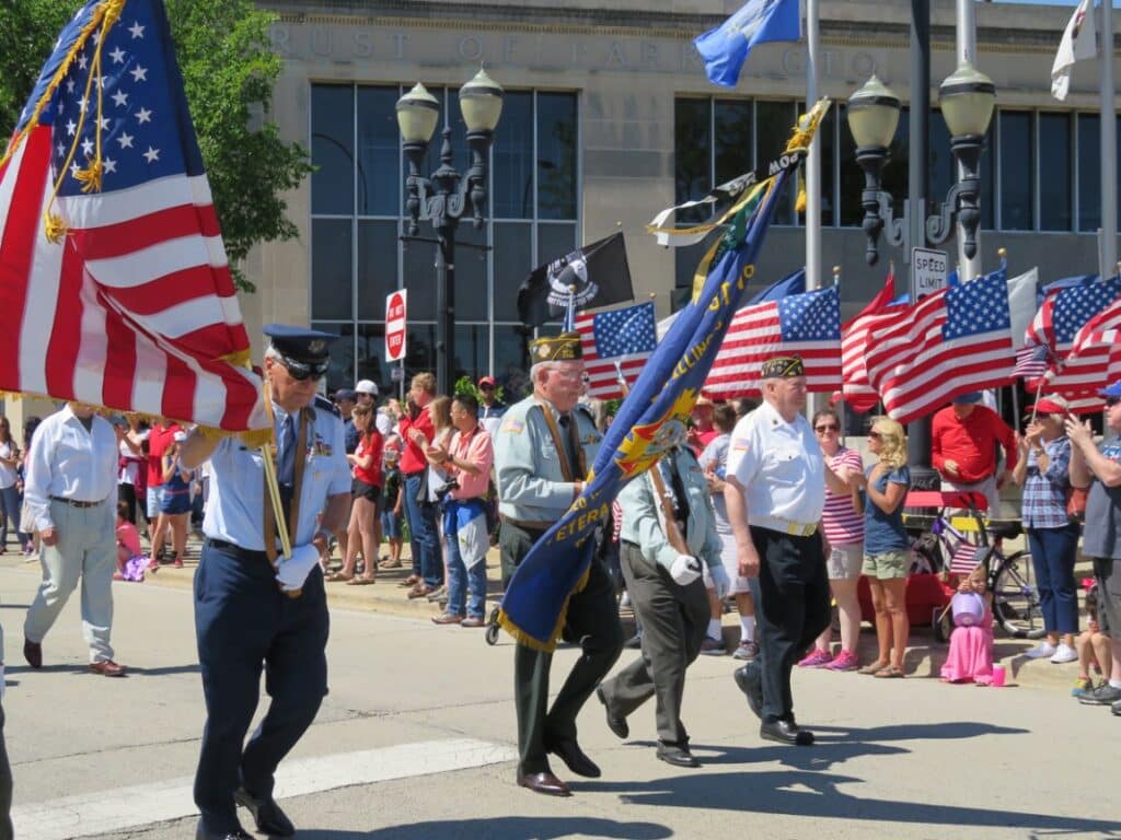 image of a Memorial Day parade showing servicemen marching with the American flag.